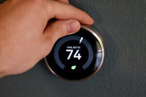 Hand adjusting temperature on smart thermostat to save energy and money.