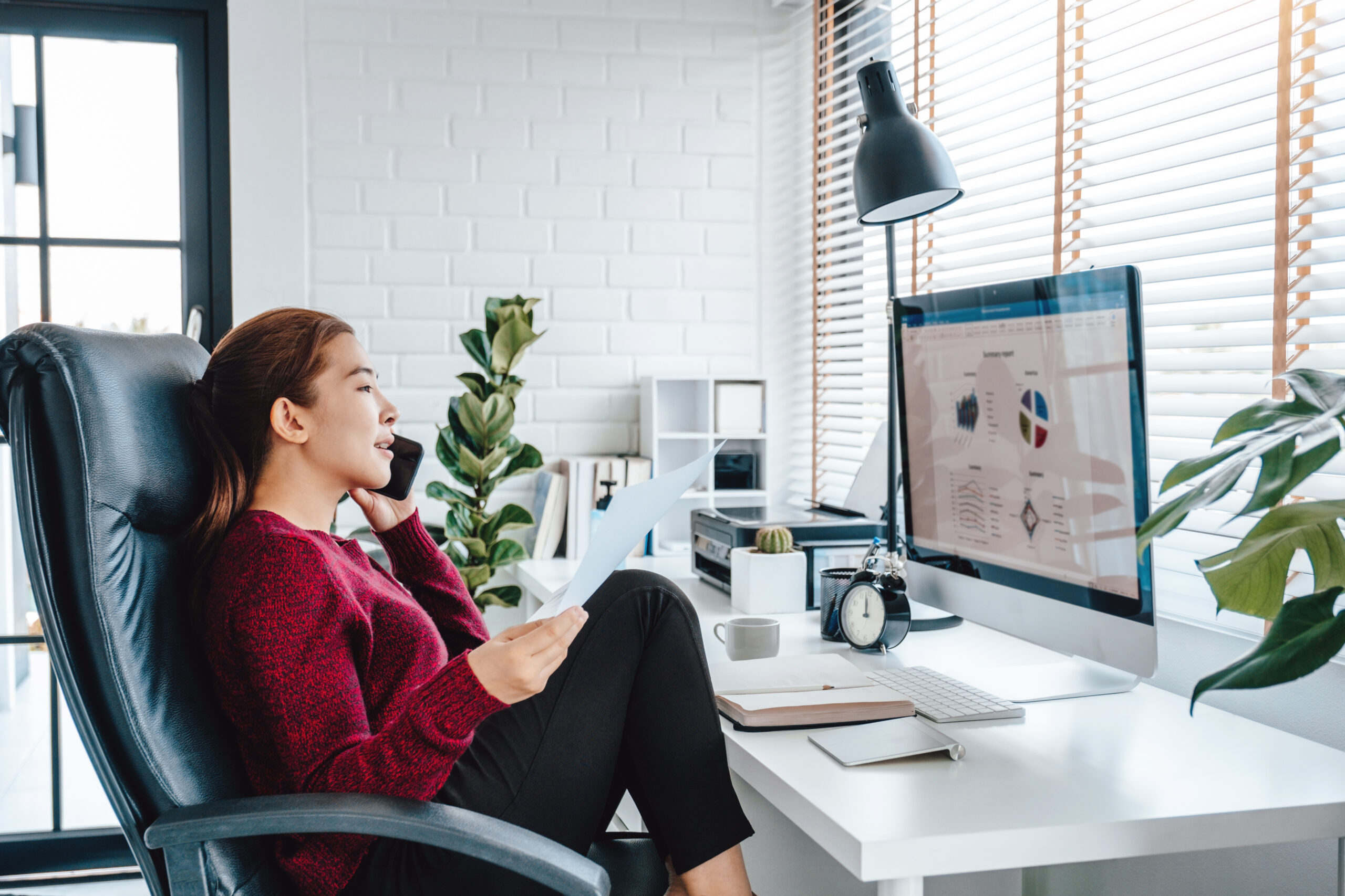 Woman sitting casually in a home office chair talking on a cell phone and working from home