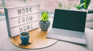 "work from home" light box next to a laptop and coffee cup with a sunlit window behind