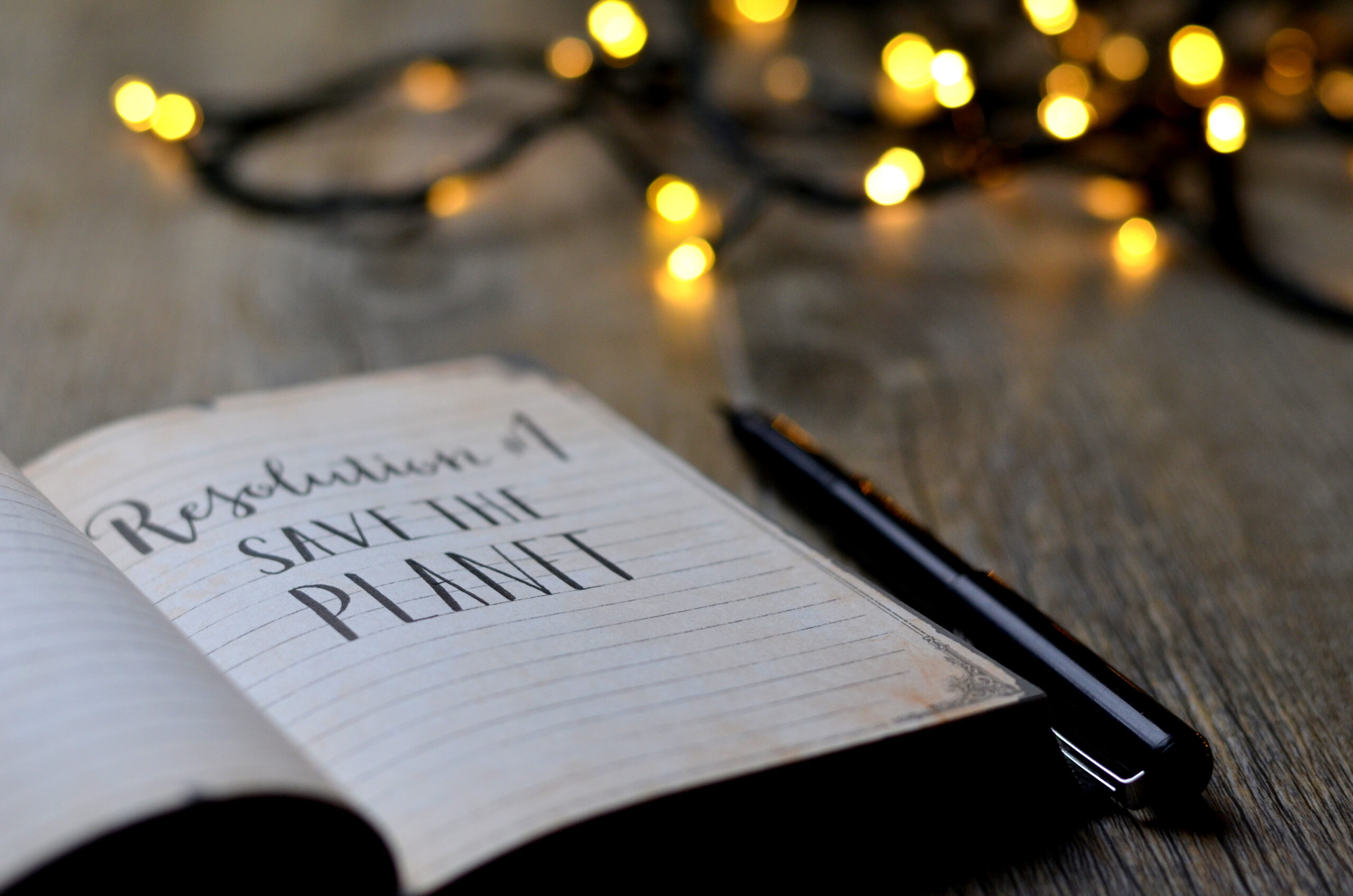 open notebook on a desk with the words "Resolution #1 - Save The Planet" written in black ink.