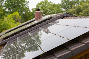 Tile roof surface of house with glossy-black solar panels installed for green energy