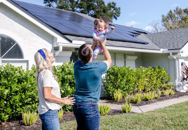 happy couple with daughter in the arms of a father in front of a home with solar celebrating their pearl certification value