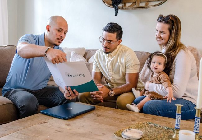 Solcium Solar's energy consultant shows a folder of solar information to an inquiring couple on a couch inside their home.