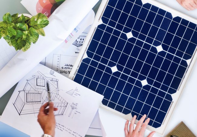 Solcium Solar team discussing the design of a solar energy system while standing over plans and drawings of the system.