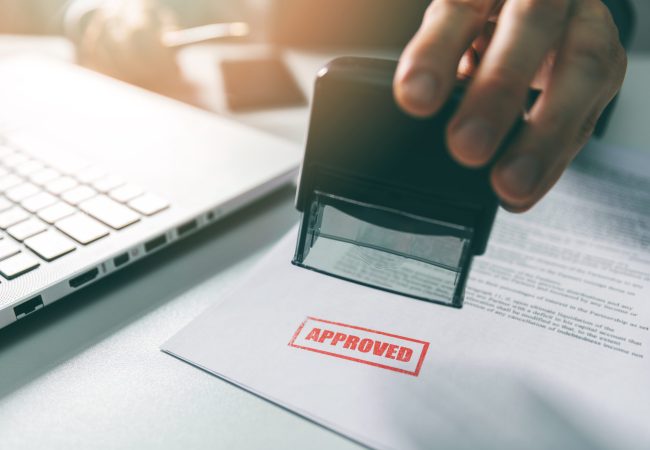 Business person stamps a permit application with a stamp that reads "Approved".