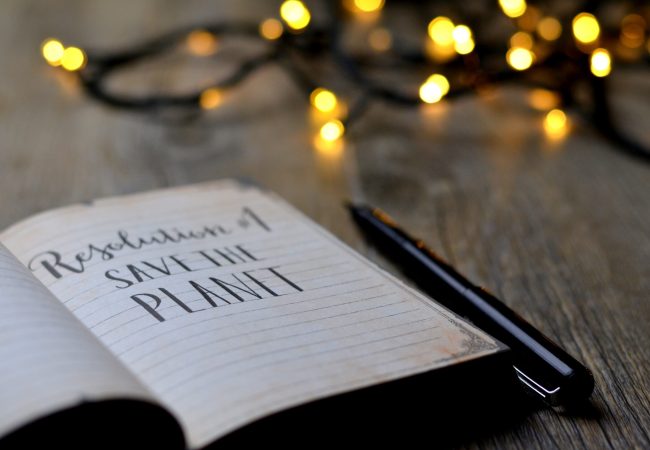 open notebook on a desk with the words "Resolution #1 - Save The Planet" written in black ink.