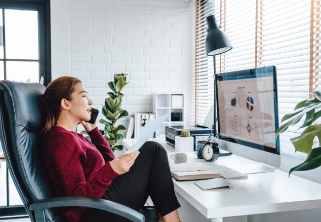 Woman sitting casually in a home office chair talking on a cell phone and working from home