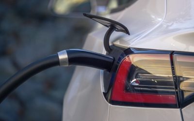 Electric car charging at charging station outdoors, closeup on power plug cord connected to charging port.