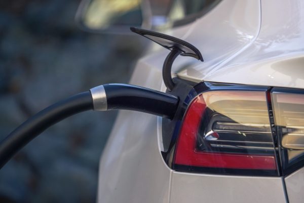 Electric car charging at charging station outdoors, closeup on power plug cord connected to charging port.